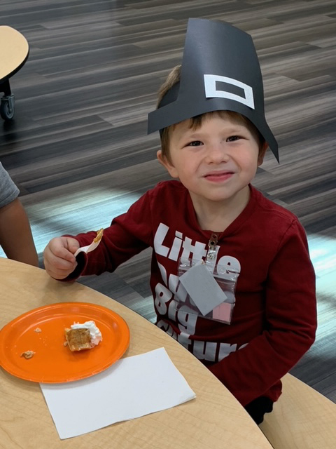 Student wearing a pilgrim hat and eating pie. 