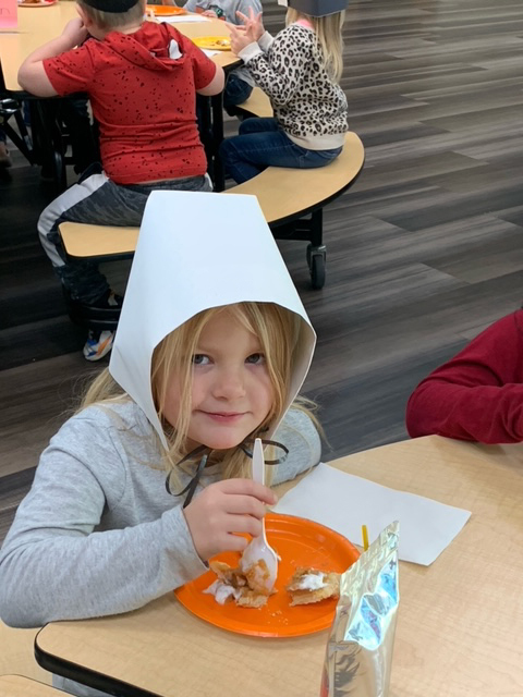 Student wearing a pilgrim hat and eating pie. 