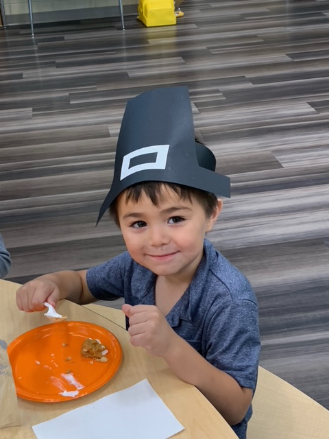 Student wearing a pilgrim hat and eating pie. 