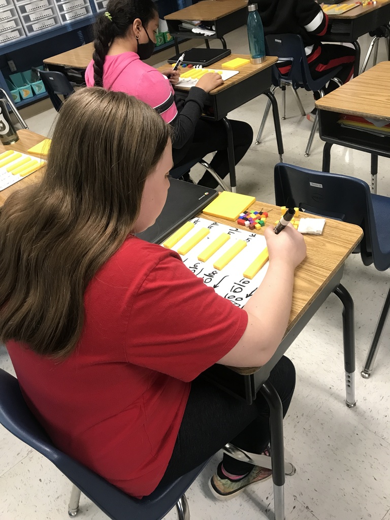 Student at desk working on math problems on white board. 