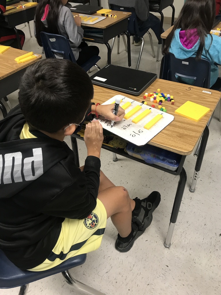 Student at desk working on math problems on white board. 