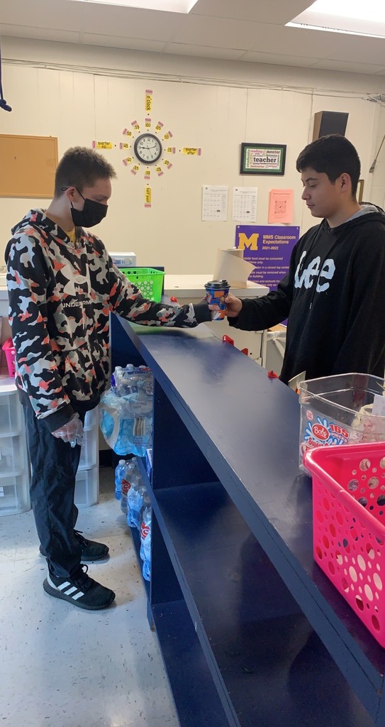 Student hands hot chocolate to another student.