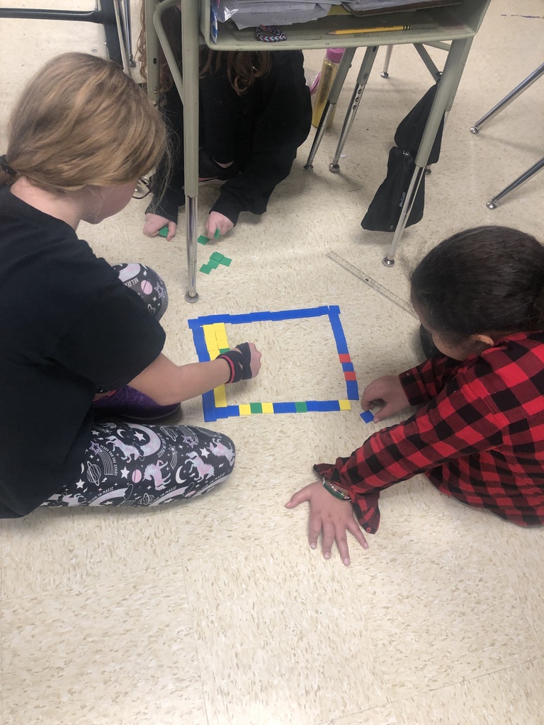 Two students sitting on the ground working on their math problems with tiles.