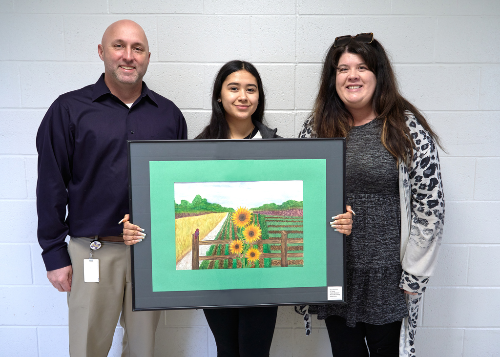 Student holds her art display with superintendent on left side and Mrs. Wallsmith on right side. 