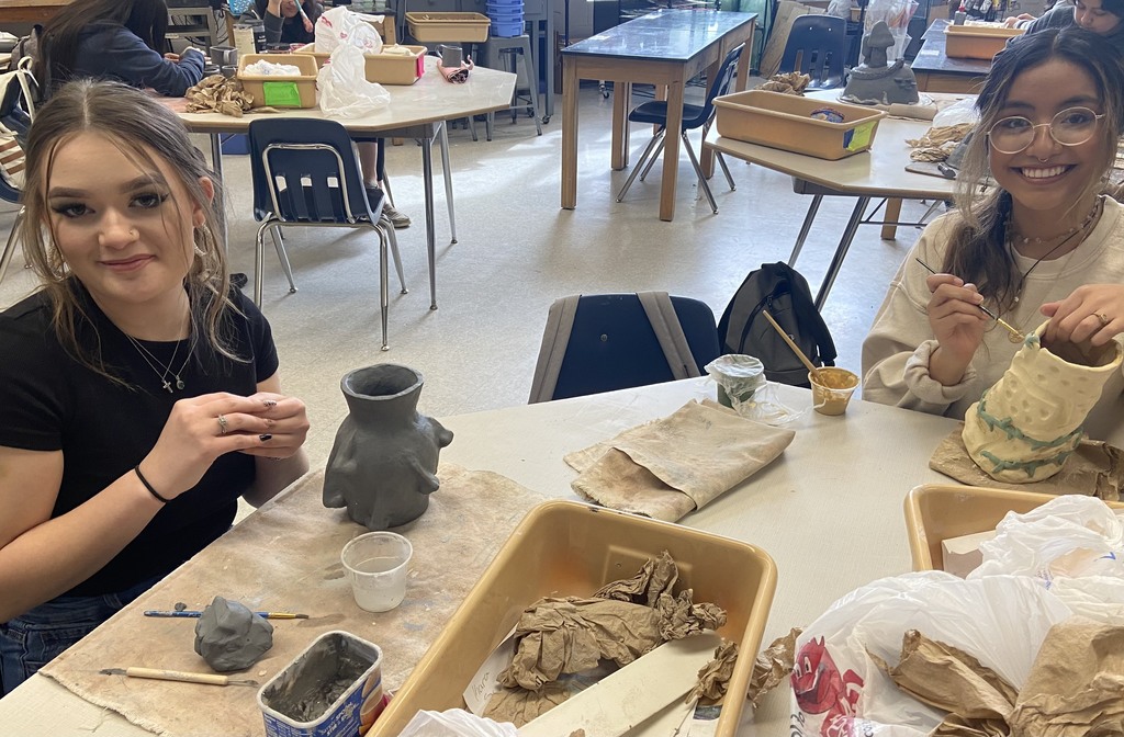 Two female students sitting next to each other working on ceramics project. 