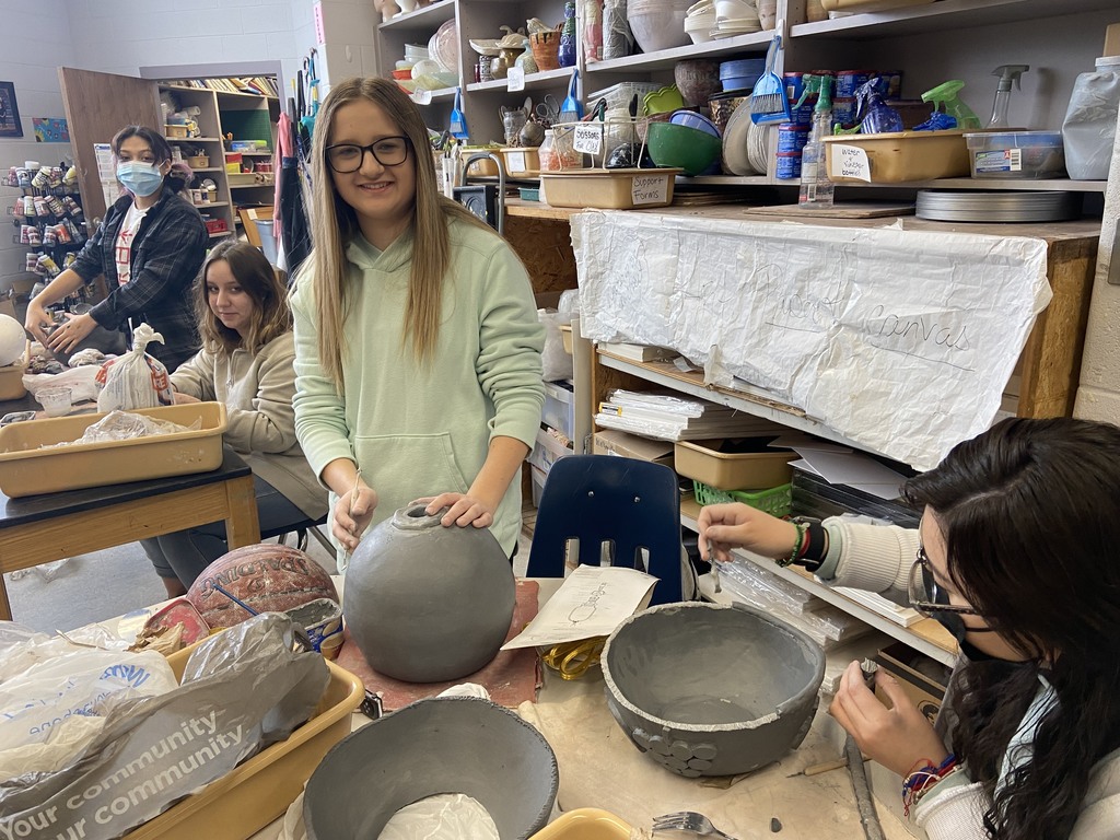 Female student wearing green hoodie is workin on her ceramics art project. 