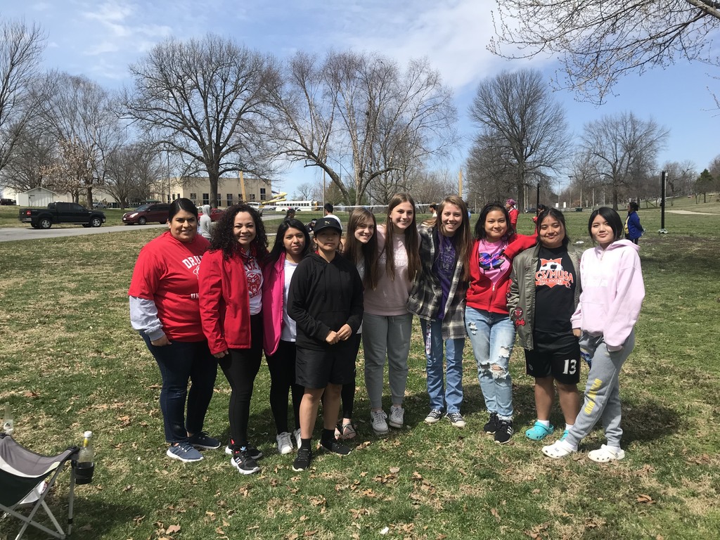 Group of female students standing for a photo while the soccer tournament is playing in the back. 