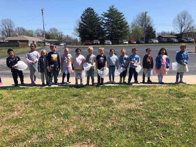 Students standing on side walk, holding white plastic bags, getting ready to take off for the easter egg hunt. 
