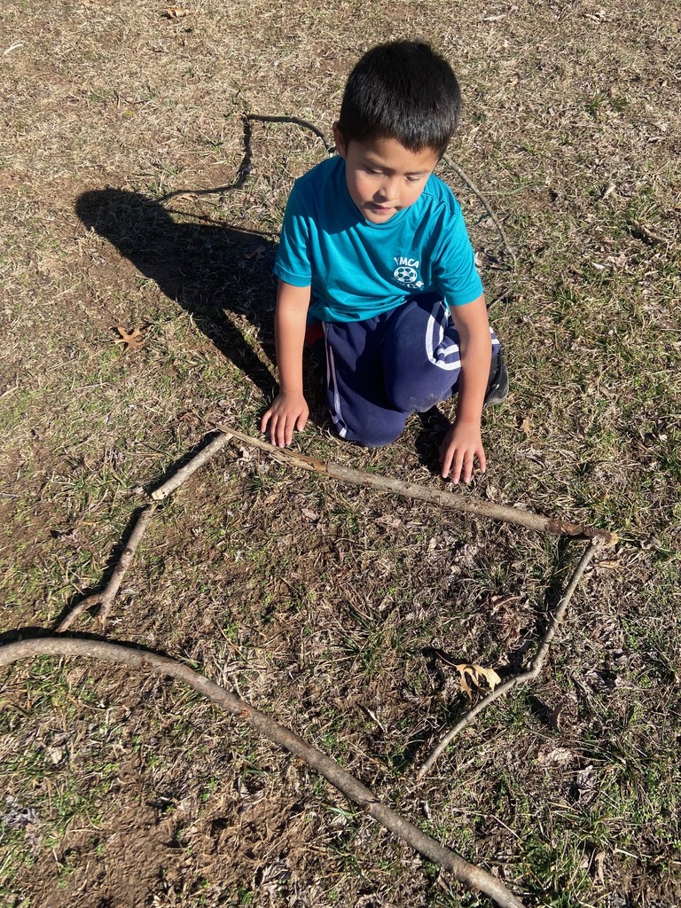 Boy with a blue shirt on building a shape out of sticks on the ground. 