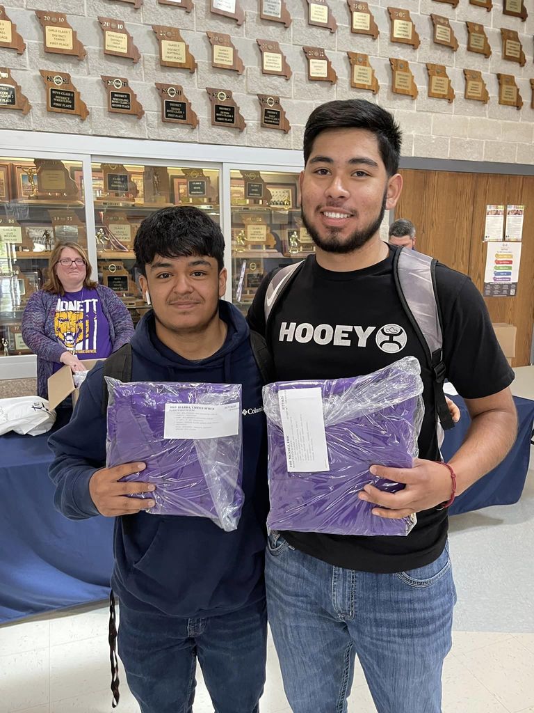 Two male student hold cap and gown for photo. 