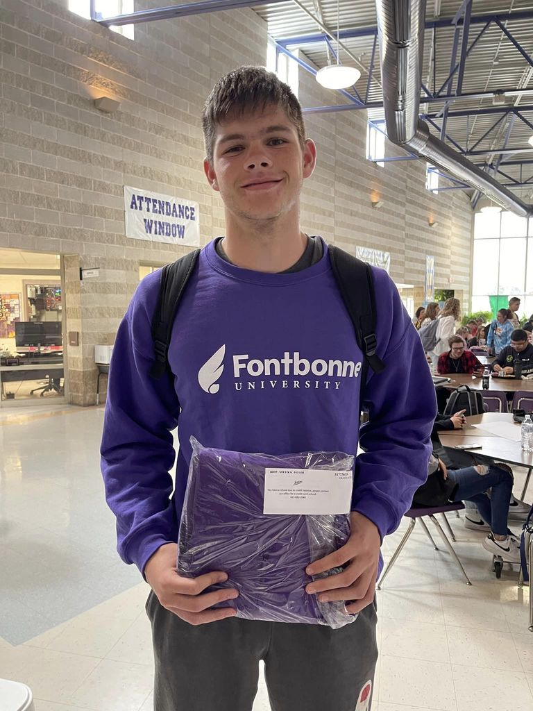 Male student holds cap and gown for photo. 