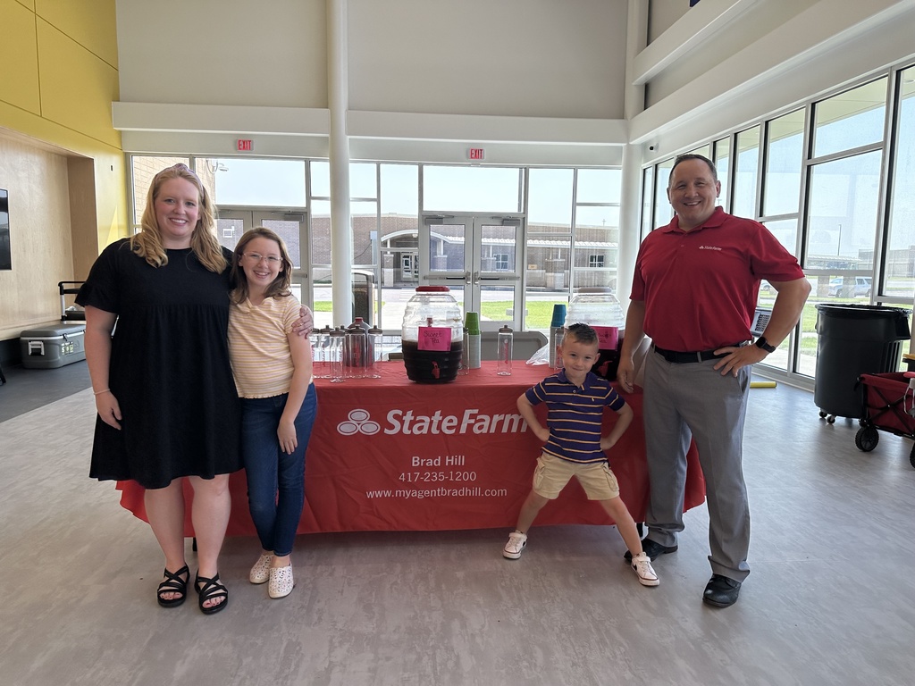 Family standing in front of the State Farm table with beverages on the table. 
