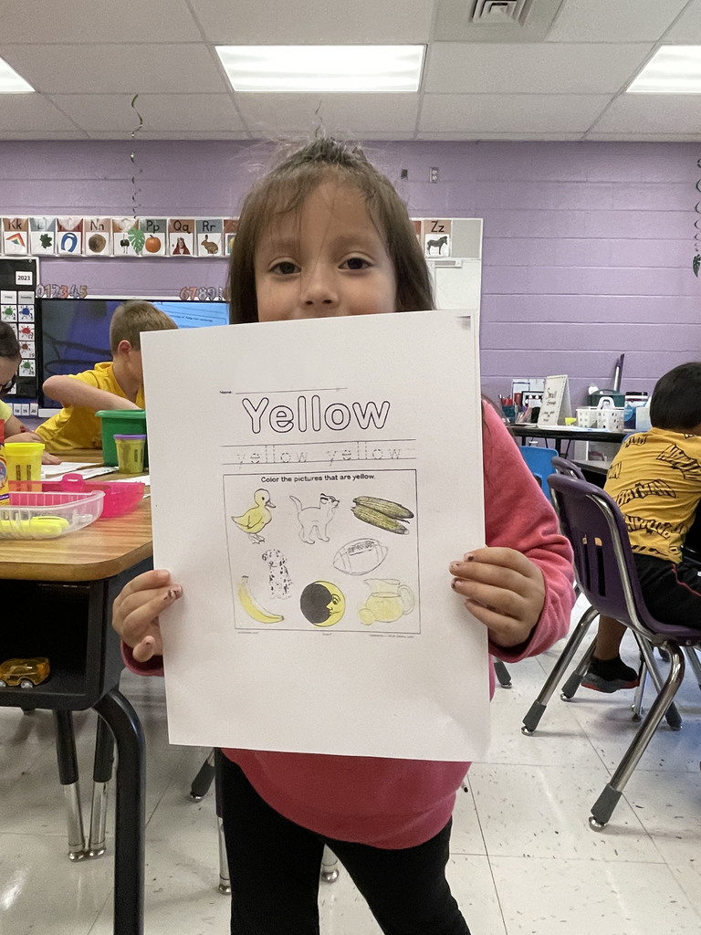 Girl student holding her paper after she colored it with the a yellow crayon.