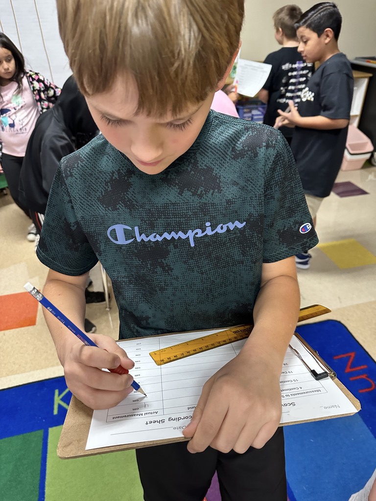 Student wearing a blue and black shirt holds a clipboard to work on math.