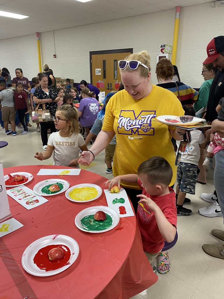 Students painting with apples, the paint colors are red, green, yellow. The mother is wearing a yellow Monett school shirt. 