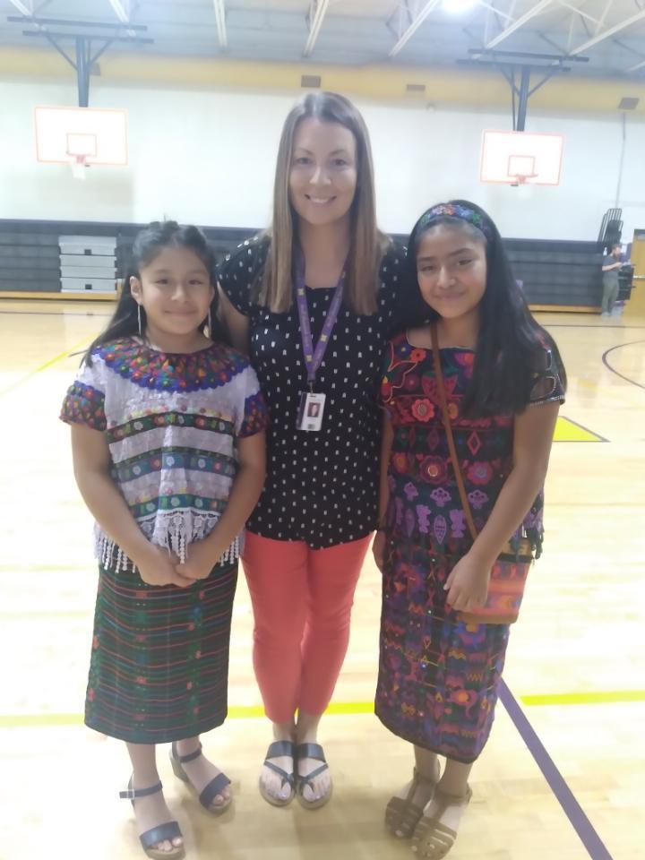 The teacher stands in between two students wearing their Guatemalan attire. 