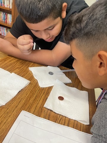 Two boys work on their coin experiment on the school desk.